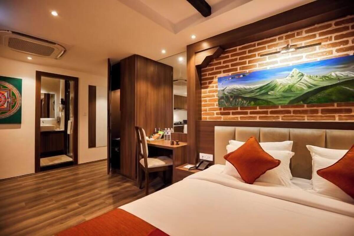 A hotel room with a bed, a desk, a chair, and a painting on the wall.