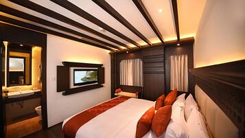 A hotel room with a large bed, a television mounted on the wall, a bathroom with a sink and toilet, and a wooden ceiling with exposed beams.