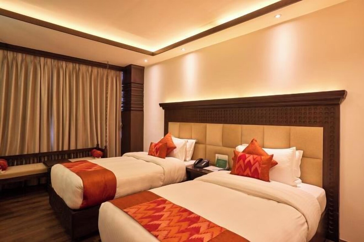 Quarto de hotel com duas camas, um banco e uma janela grande com cortinas.