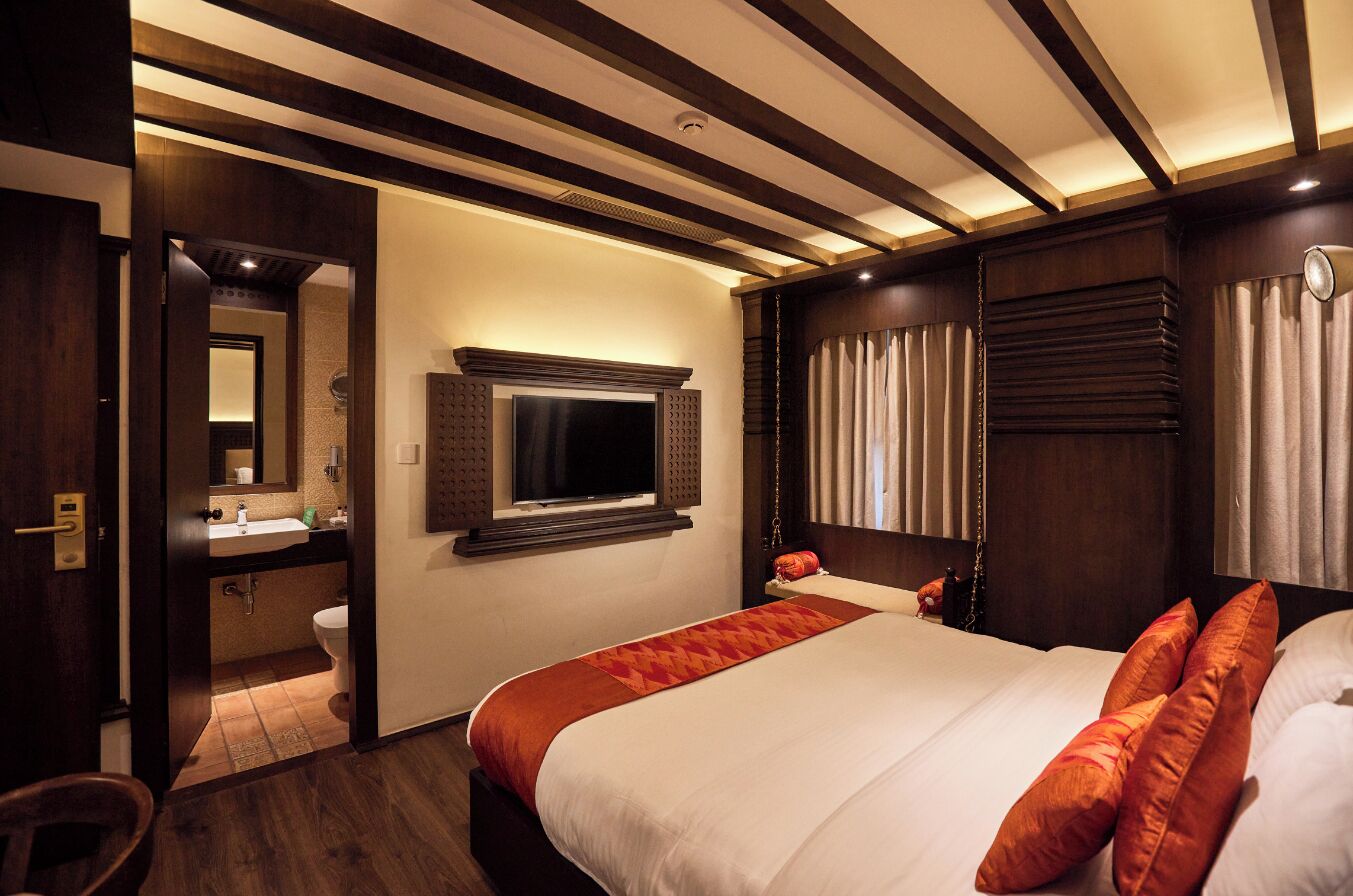 A hotel room with a large bed, a bedside table, a mirror, a window with curtains, and a bathroom visible through an open door.