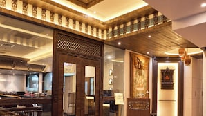 A spacious hotel lobby with a large wooden reception desk, a decorative ceiling, and a tiled floor. - Kantipur Village (Kathmandu)