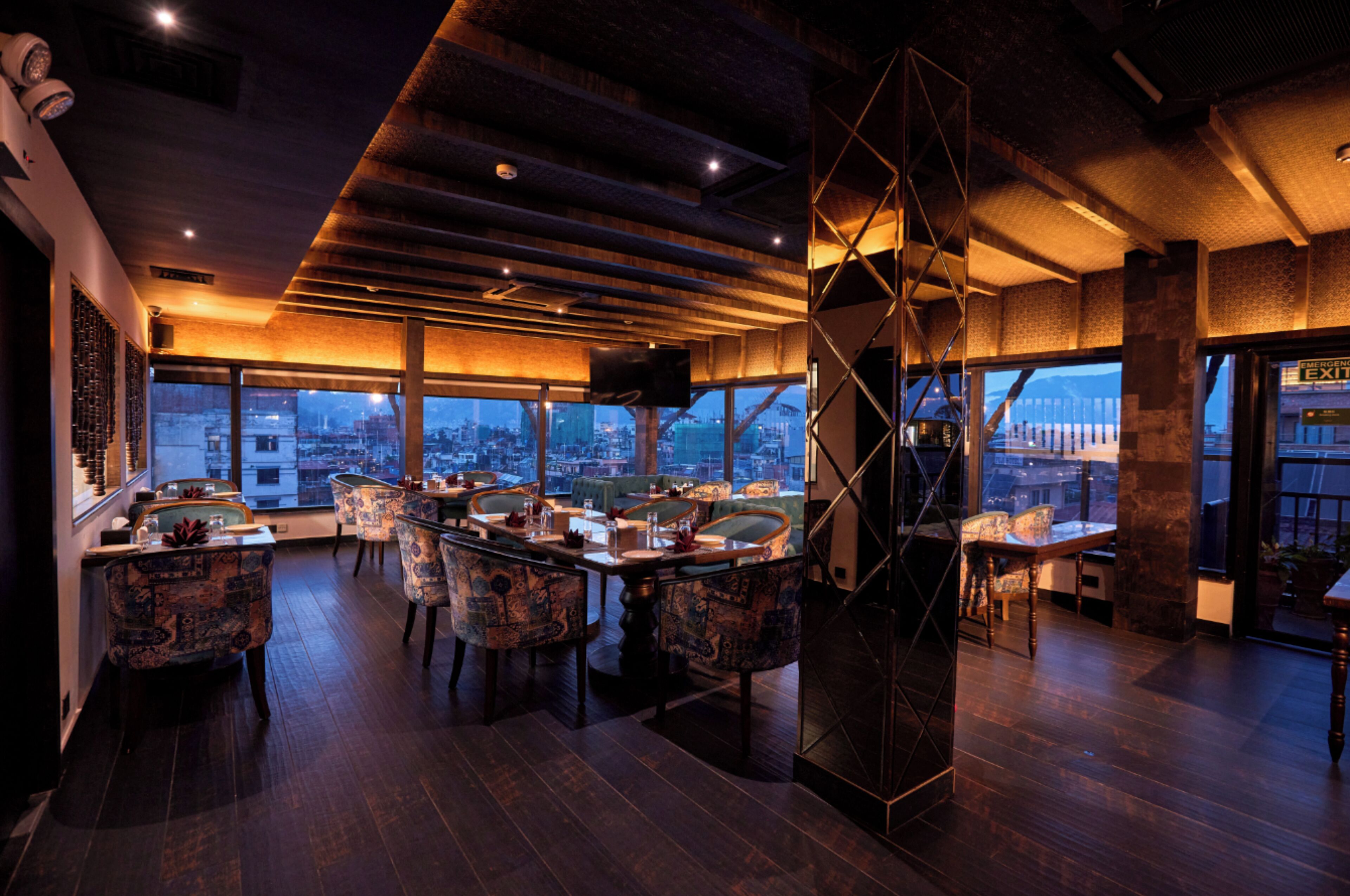 Restaurante moderno com vista para a cidade, piso de madeira e cadeiras estampadas.