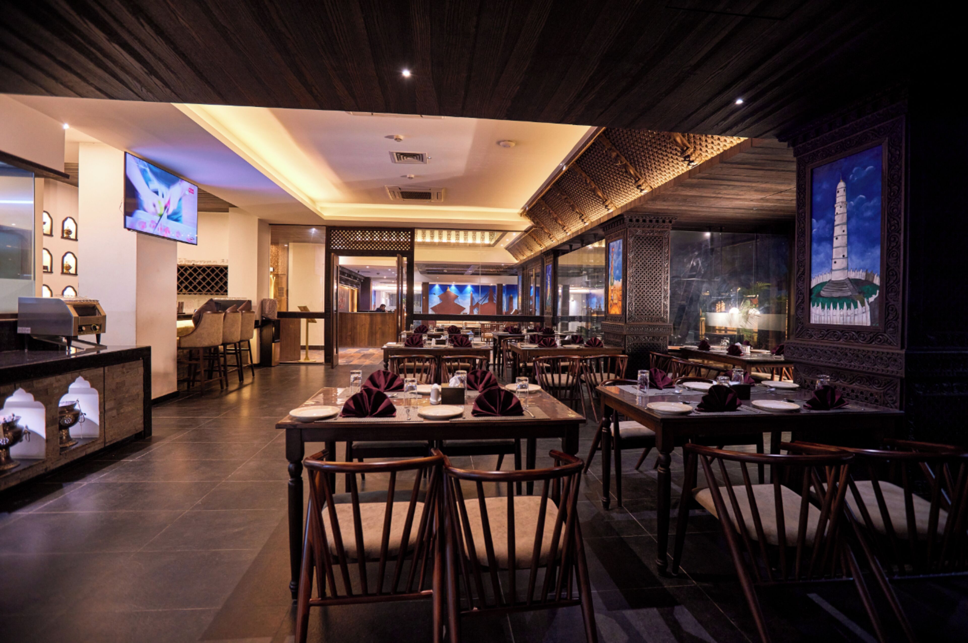 A restaurant with multiple dining tables and chairs, a bar area, and a large window with a view.