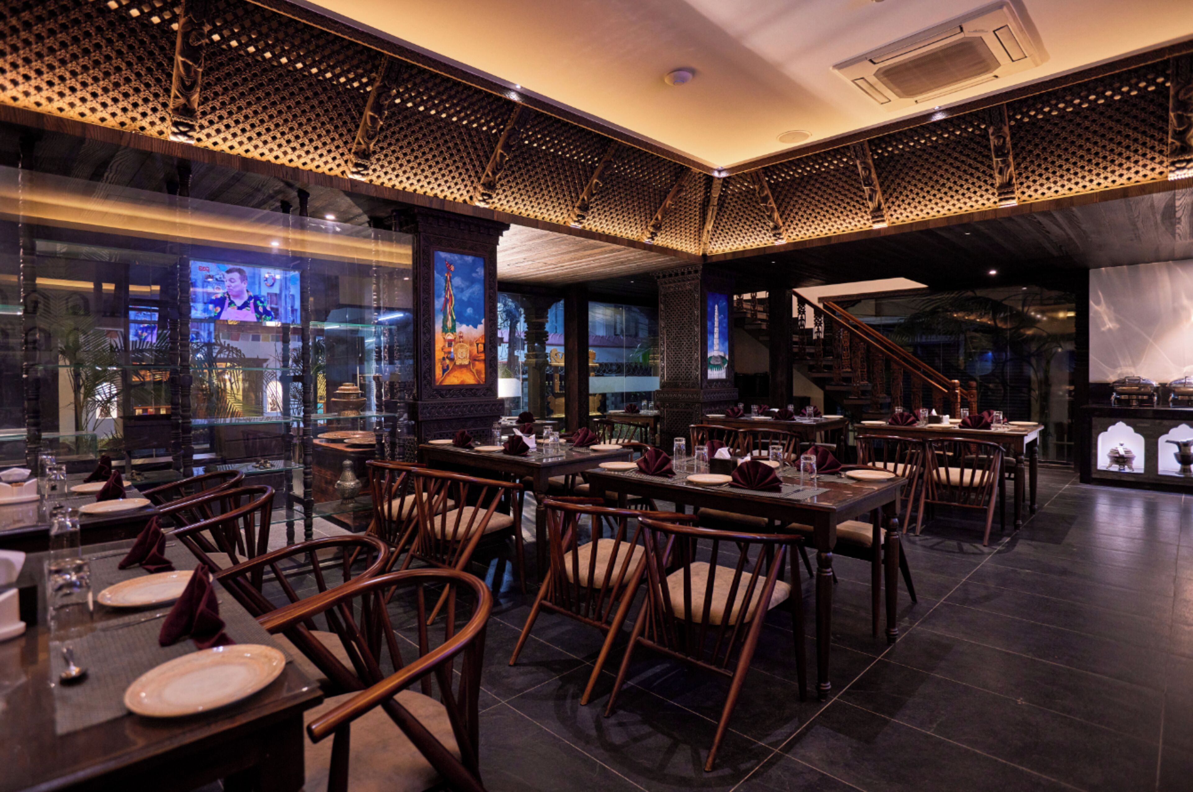 A restaurant with multiple dining tables and chairs, a staircase, and a large window displaying a cityscape.