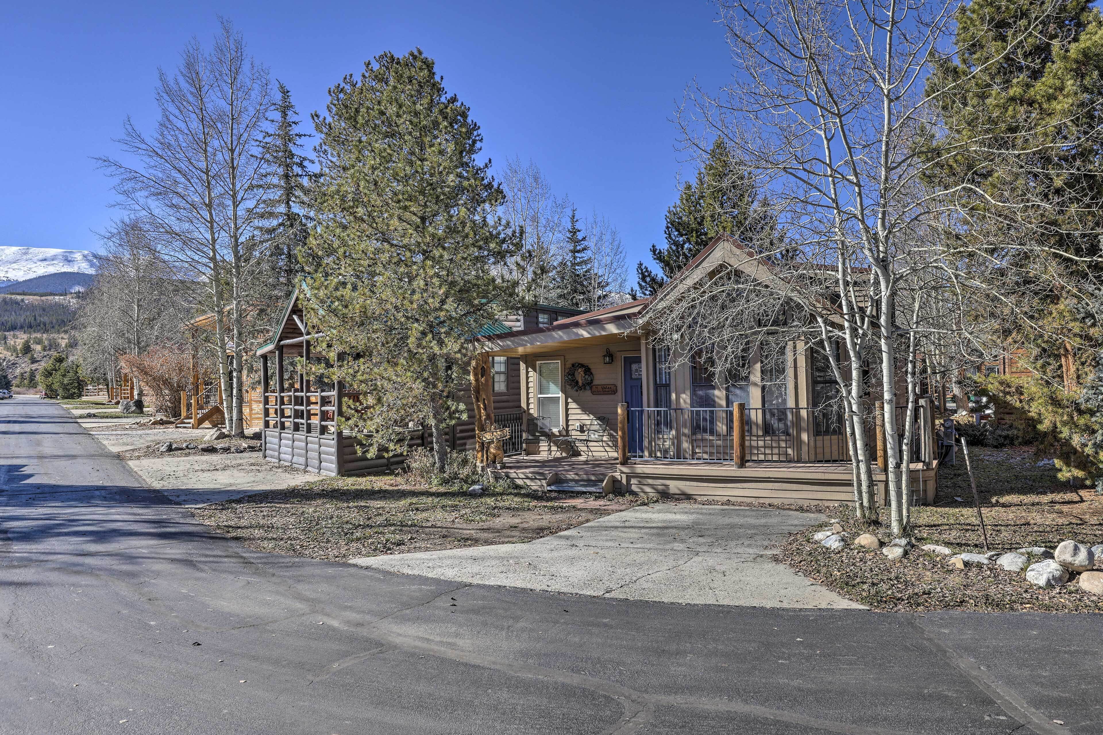 A single-story log cabin with a front porch, surrounded by trees and a clear sky.