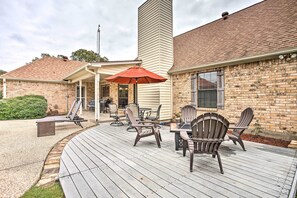 Un patio couvert, aménagé avec du mobilier d’extérieur, notamment des chaises et une table, et agrémenté d’un parasol rouge.