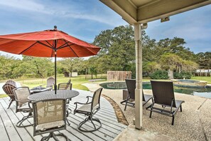 Une terrasse extérieure avec une table ronde et des chaises, un parasol rouge et un espace piscine.