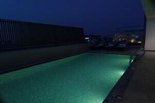 A rooftop pool area with a clear view of the sky, a wooden fence, and lounge chairs.