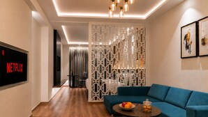 A modern living room with a blue sofa, a coffee table with fruit and cookies, a TV displaying 'NETFLIX,' and a decorative white partition. - Regenta Place Amritsar (Amritsar)