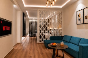 A modern living room with a blue sofa, a coffee table with fruit and cookies, a TV displaying 'NETFLIX,' and a decorative white partition. - Regenta Place Amritsar (Amritsar)