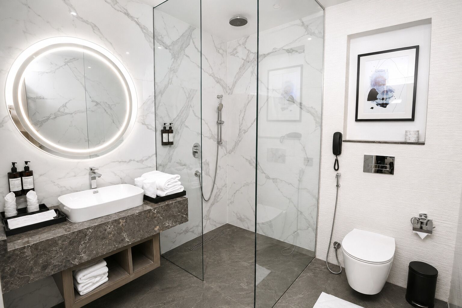 Une salle de bain moderne avec un meuble-lavabo en marbre, un miroir rond, une douche et des toilettes.