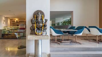 Um interior moderno com uma estátua de uma divindade em um pedestal, uma vitrine de vidro e uma área de estar com cadeiras azuis e brancas.