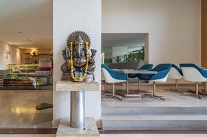 Um interior moderno com uma estátua de uma divindade em um pedestal, uma vitrine de vidro e uma área de estar com cadeiras azuis e brancas.