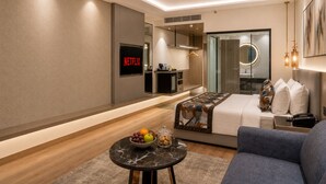 A modern hotel room with a bed, a sofa, a small table with fruit, a TV displaying 'NETFLIX,' and a mirror. - Regenta Place Amritsar (Amritsar)