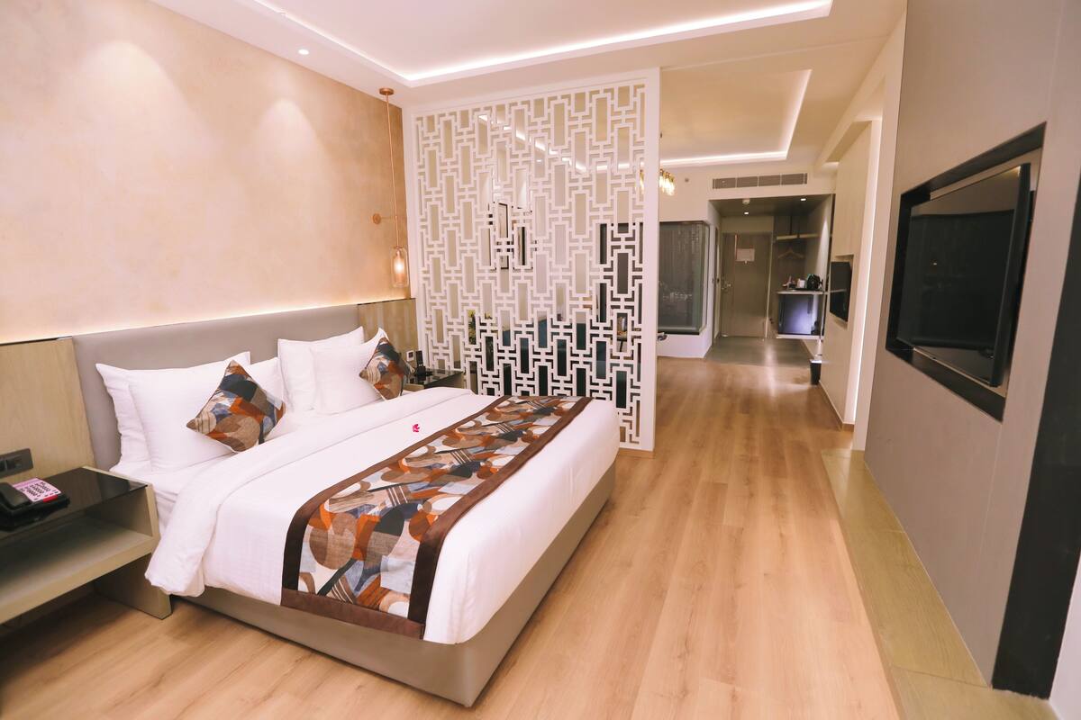 Ein modernes Hotelzimmer mit einem großen Bett, einem Nachttisch mit Telefon, einer Zierverkleidung an der Wand und einem an der Wand befestigten Fernseher.
