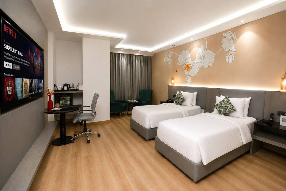 Ein Hotelzimmer mit zwei Betten, einem Schreibtisch mit Stuhl, einem an der Wand befestigten Fernseher und einer Wanddekoration.