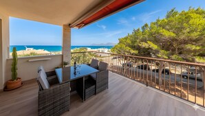 A balcony with a table and chairs, a potted plant, and a view of the sea and trees.