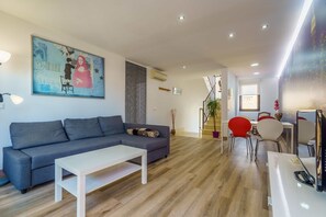 Een moderne woonkamer met een grijze bank, een witte salontafel en een eethoek met rode stoelen.