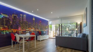 A modern living room with a cityscape mural, a dining area with red chairs, a gray sofa, and a white TV stand.