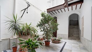 A courtyard with potted plants, a marble floor, and a staircase leading to an upper level.