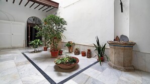 A courtyard with potted plants, a marble floor, and a stone pedestal.