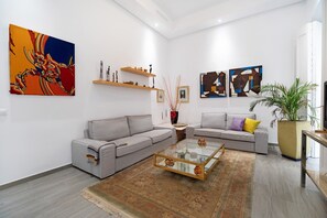 Un salon moderne avec deux canapés gris, une table basse en verre et des œuvres d’art abstraites accrochées aux murs.