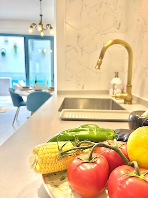 A kitchen with a marble backsplash, a gold faucet, and a variety of fresh vegetables on the counter. - Holiday Home "Recuerdos del Sur" with Pool, Terrace, Balcony, BBQ, A/C & Wi-Fi (El Gastor)