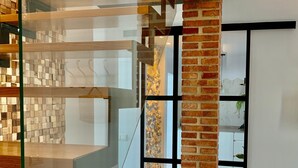 Interior moderno com escadaria de vidro, coluna de tijolo e piso estampado.