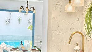 Cozinha moderna com painel de fundo de mármore, torneira dourada e área de jantar com cadeiras azuis e vista para a piscina.