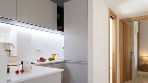 Una cocina moderna con armarios blancos, horno integrado y una encimera con utensilios de cocina y frutas.