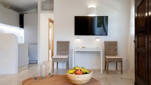 Una sala de estar moderna con una mesa de madera, un frutero, dos sillones de mimbre, una consola blanca y un televisor de pantalla plana montado en la pared.