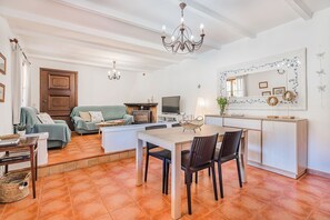A living room with a sofa, a dining table with chairs, a TV, and a kitchen area with a fridge and microwave.