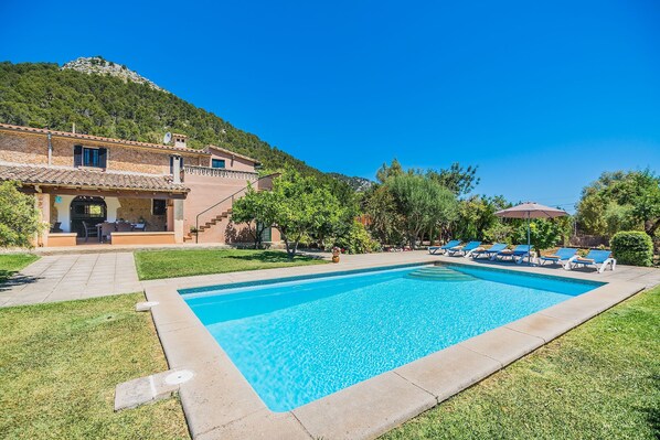Une piscine avec des chaises longues, un espace patio et un bâtiment dont l’arrière-plan est constitué d’une chaîne de montagnes.