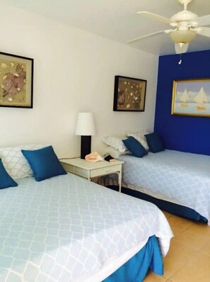 A hotel room with two beds, a ceiling fan, and artwork on the walls.