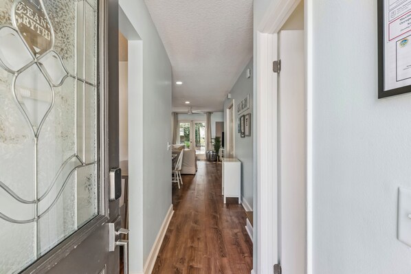 A hallway with a wooden floor, a glass door with a decorative pattern, and a white wall with a framed certificate.