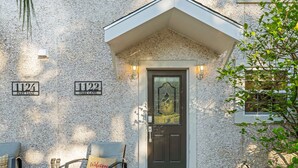 Une maison avec une façade en pierre, une porte d’entrée sombre et deux chaises à l’extérieur.