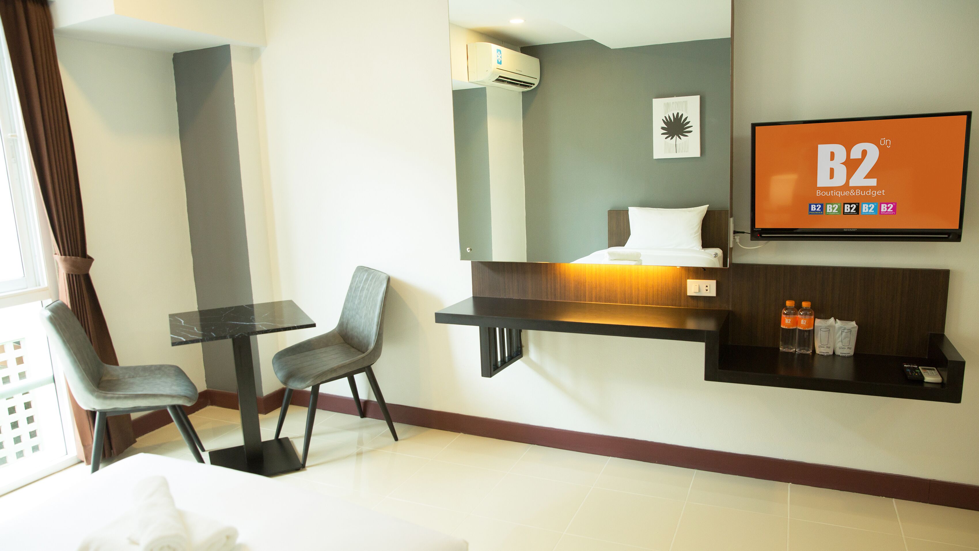 A hotel room with a bed, a desk, two chairs, a TV, and a shelf with toiletries.