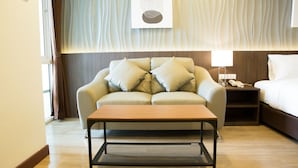 Quarto de hotel com sofá, mesa de centro, cama, mesa de cabeceira e uma obra de arte na parede.
