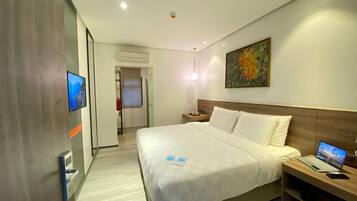 A modern hotel room with a large bed, a desk with a laptop, a TV mounted on the wall, and a painting above the bed.
