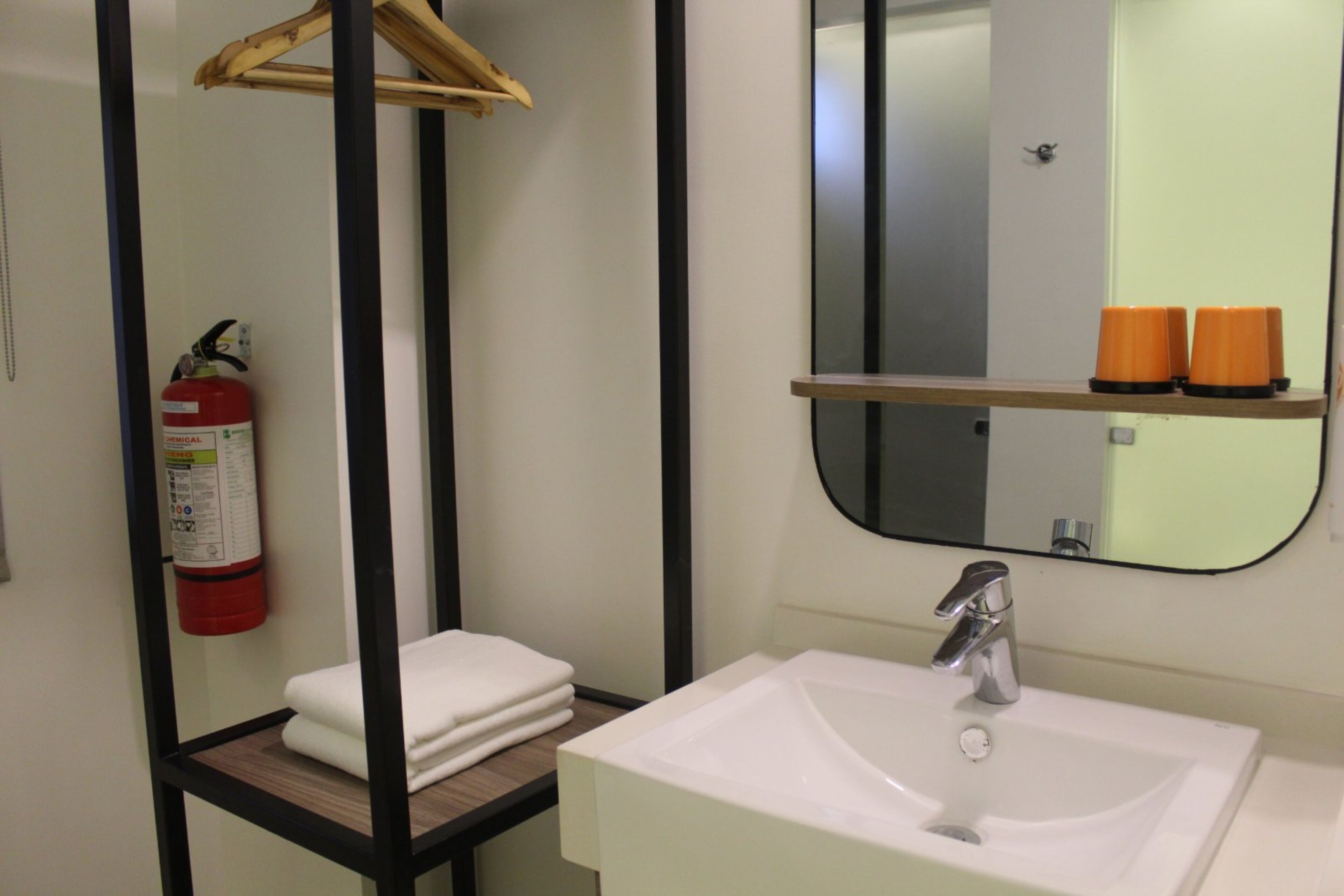 A bathroom with a white sink, a mirror, and a fire extinguisher on the wall.