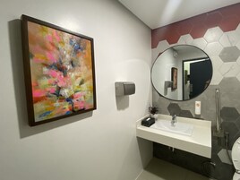 Un baño con un lavamanos blanco, un espejo redondo, un dispensador de jabón manual y un salpicadero de azulejos hexagonales.