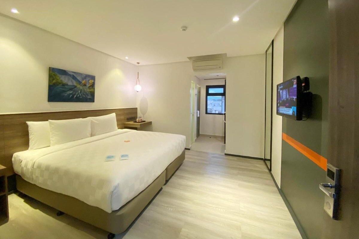 A hotel room with a large bed, a TV on the wall, and a painting on the wall.