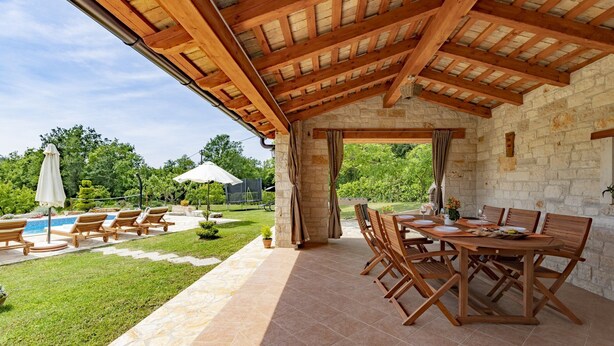 A covered outdoor patio with stone flooring, wooden tables and chairs, and a pool area in the background. - Pure relaxation - country house with pool (Karojba)