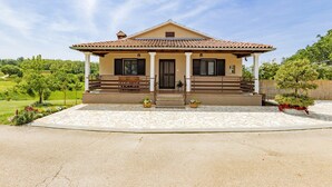 A two-story house with a tiled roof, a front porch with benches, and a garden with flowers and shrubs. - Pure relaxation - country house with pool (Karojba)