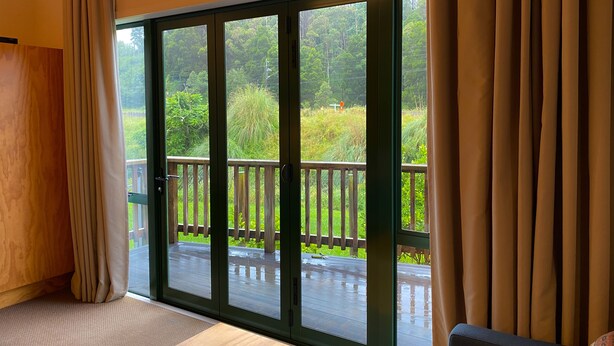 A room with a large sliding glass door leading to an outdoor deck with a wooden railing. - Waitomo Lodge (Te Kuiti)