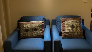 Two blue armchairs with patterned cushions, a small wall-mounted light, and a wooden table in a room with beige walls. - Waitomo Lodge (Te Kuiti)