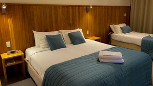 A hotel room with a large bed, a smaller bed, wooden paneling on the walls, a nightstand with a phone, and a window with curtains. - Waitomo Lodge (Te Kuiti)