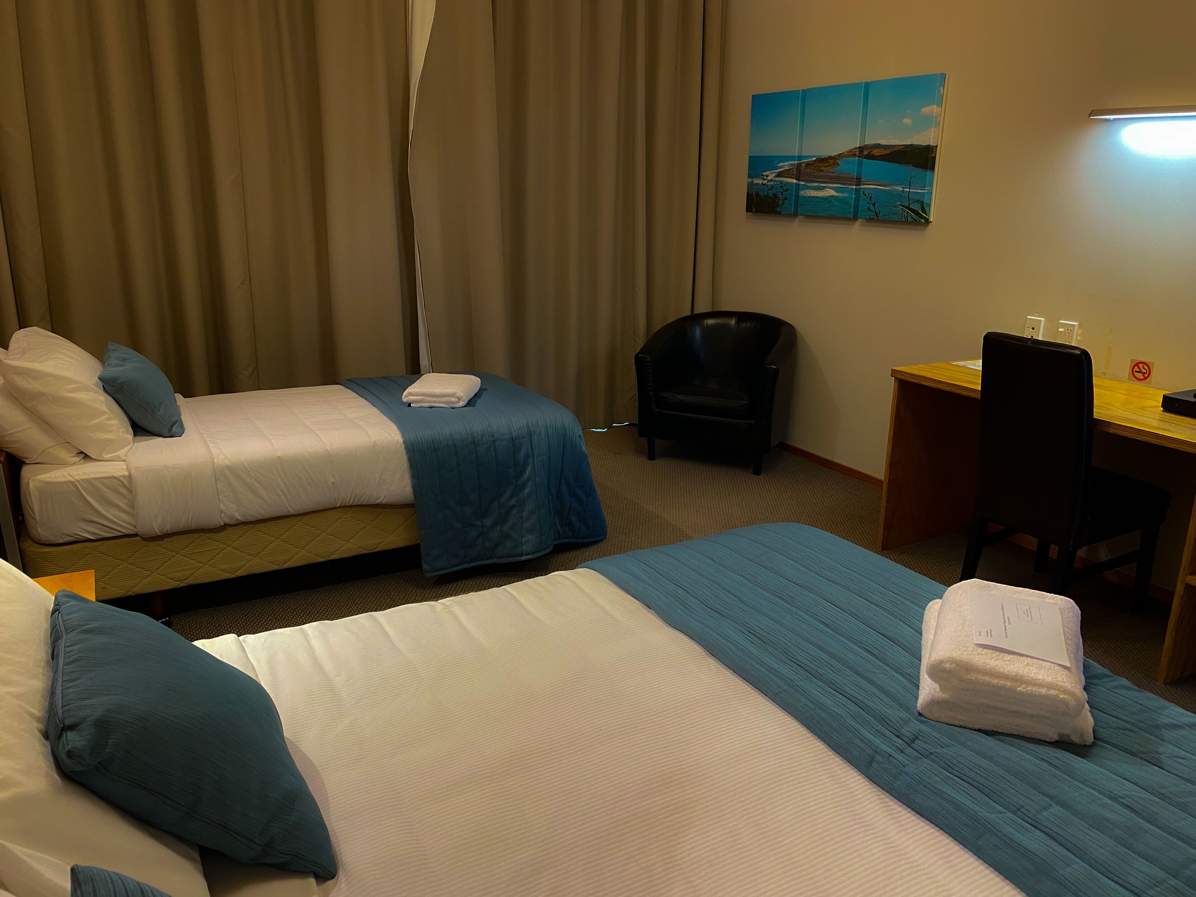 A hotel room with two beds, a desk, a chair, and a painting on the wall.