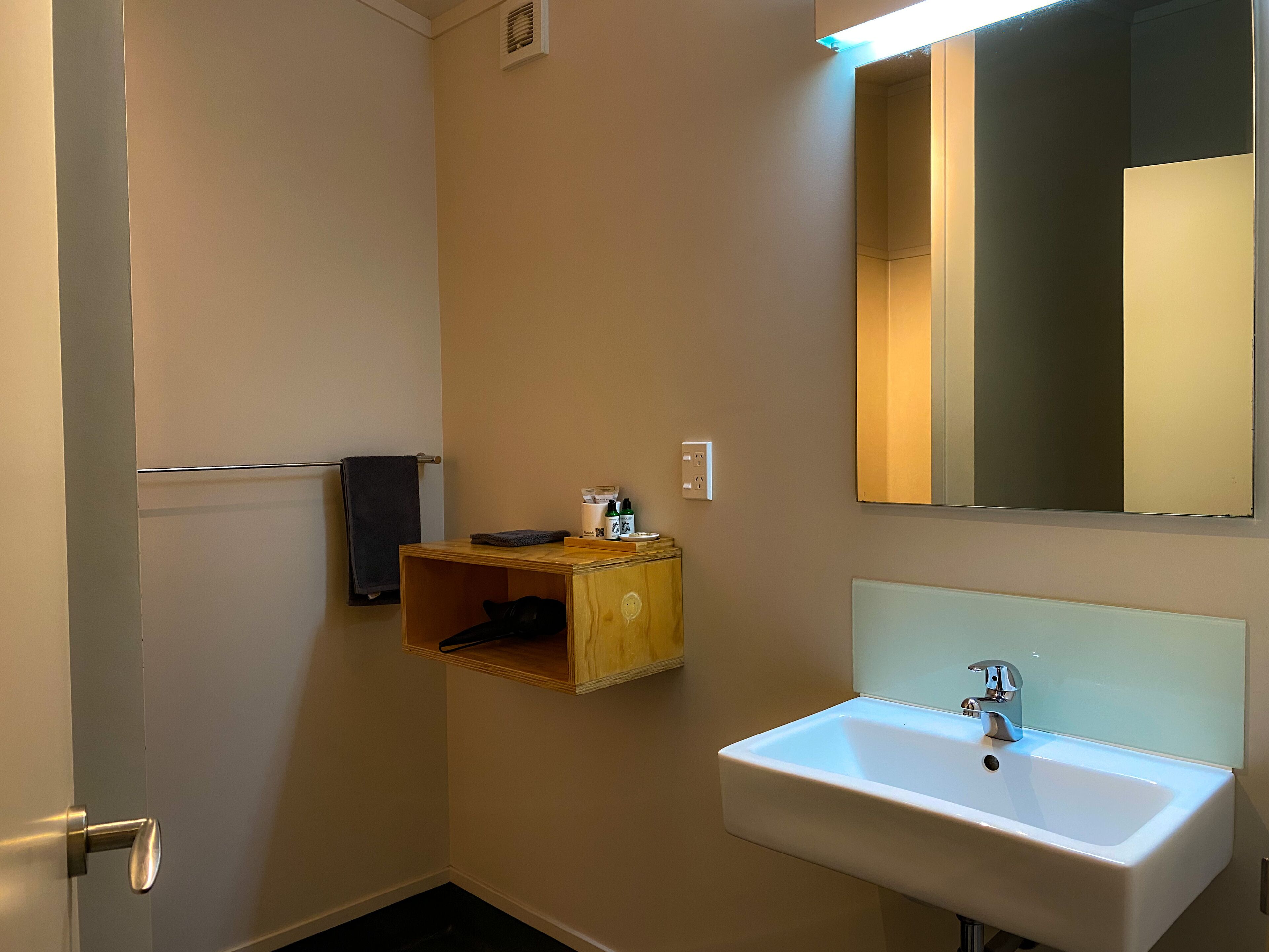 Een badkamer met een witte wastafel, een spiegel en een houten plank met toiletartikelen.