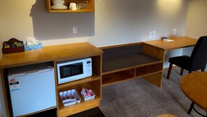 A compact kitchenette with a microwave, a small fridge, and a shelf with dishes and glasses. - Waitomo Lodge (Te Kuiti)